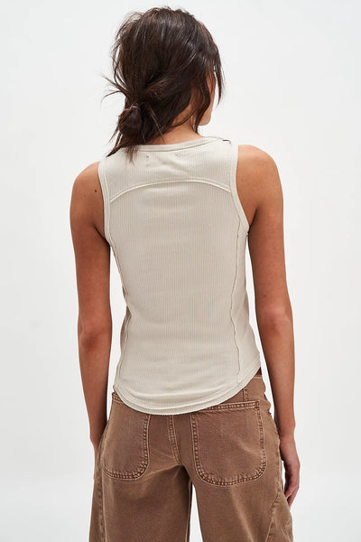 Person wearing a beige sleeveless top and brown pants on a white background