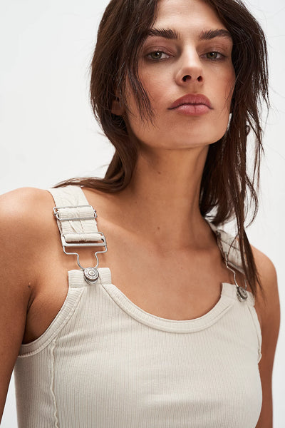 Woman wearing a beige tank top with white suspenders against a plain background