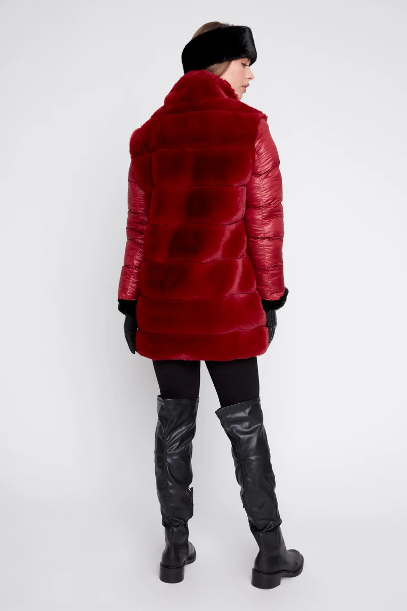 A model shown from the back wearing a vibrant red, quilted faux-fur coat with black leather boots, black pants, and a black fur hat against a plain white studio background.