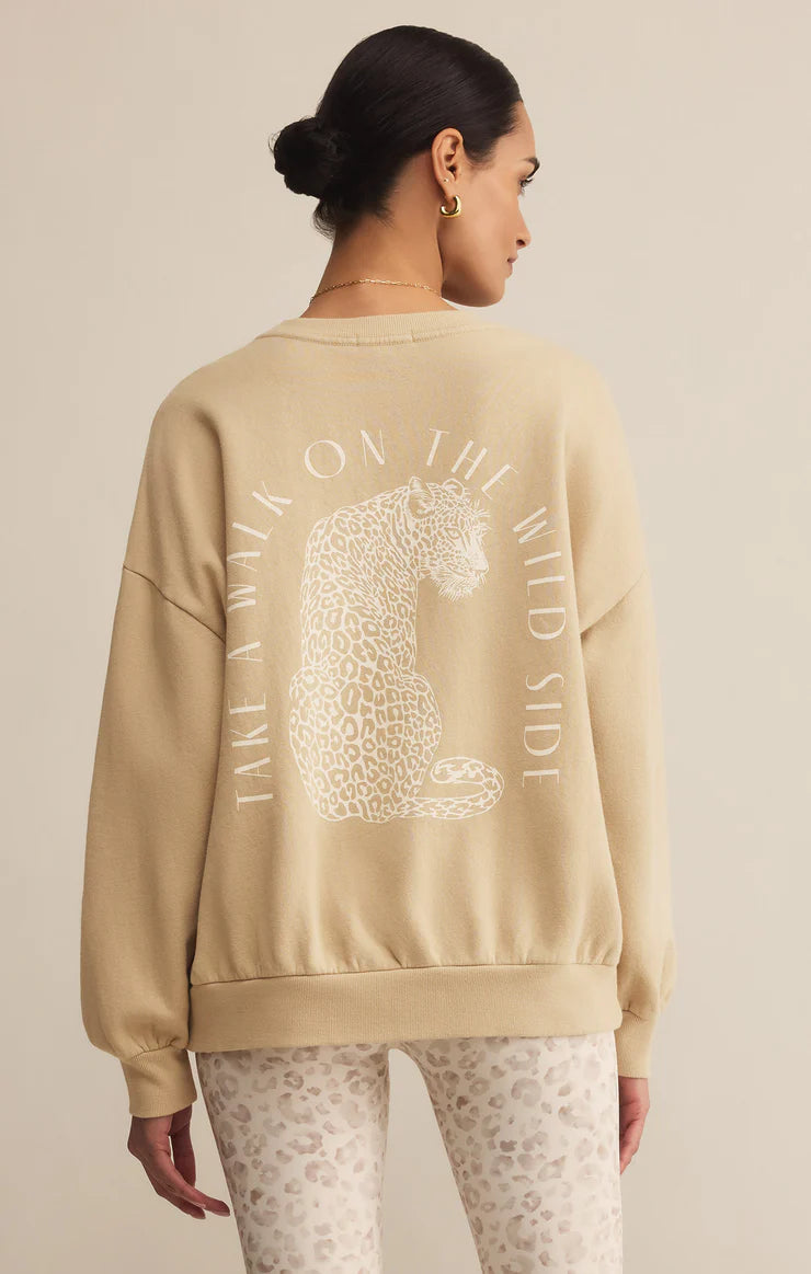 Woman wearing a beige sweatshirt with a leopard graphic and text on the back, standing against a beige background.