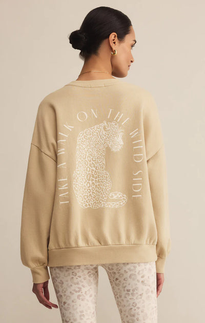 Woman wearing a beige sweatshirt with a leopard graphic and text on the back, standing against a beige background.