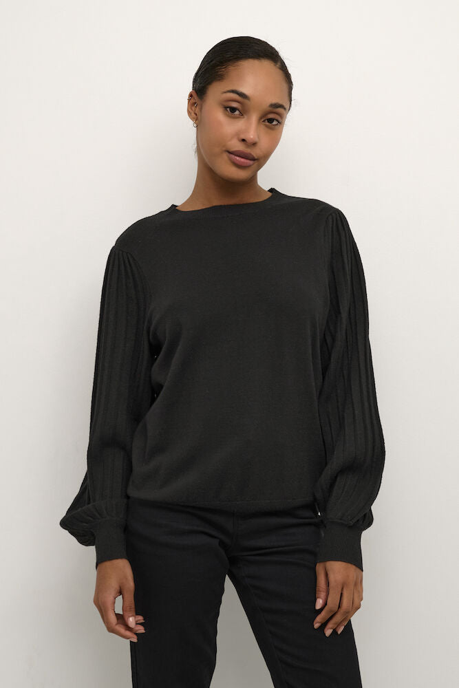 Woman wearing a black long-sleeve top and pants against a white background