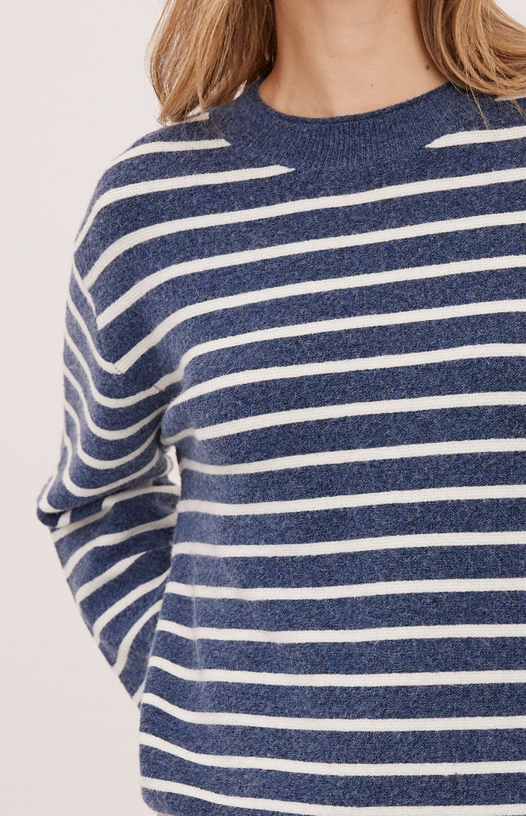 A close-up of a person wearing a knit sweater with horizontal navy blue and white stripes against a plain light background.