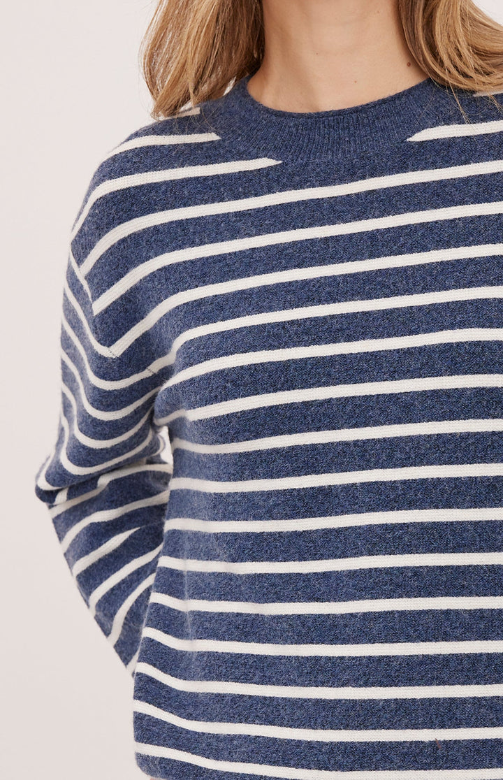 A close-up of a person wearing a knit sweater with horizontal navy blue and white stripes against a plain light background.