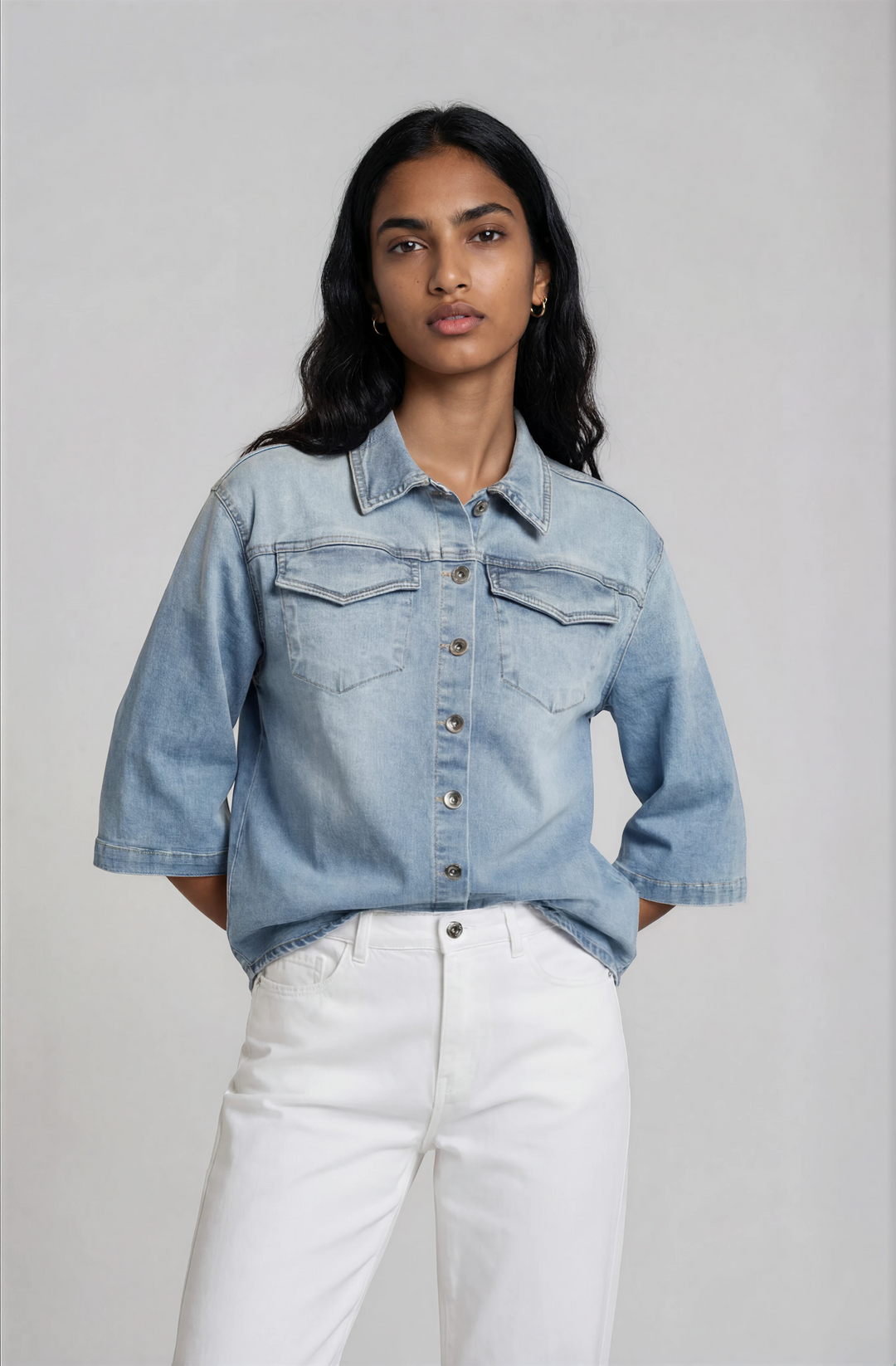 Woman wearing a light blue denim jacket and white pants against a plain background