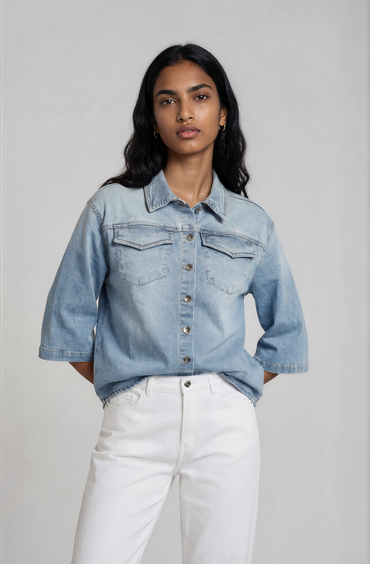 Woman wearing a light blue denim jacket and white pants against a plain background