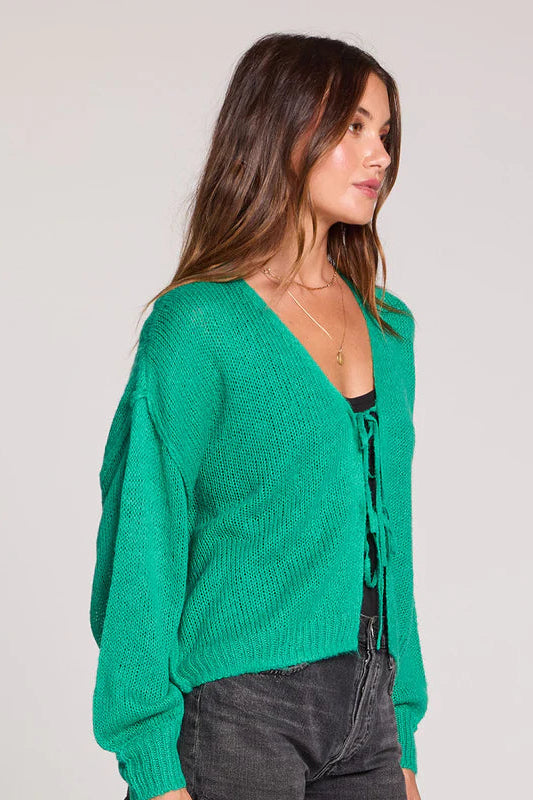Woman wearing a green cardigan with a lace-up front and black shorts on a plain background