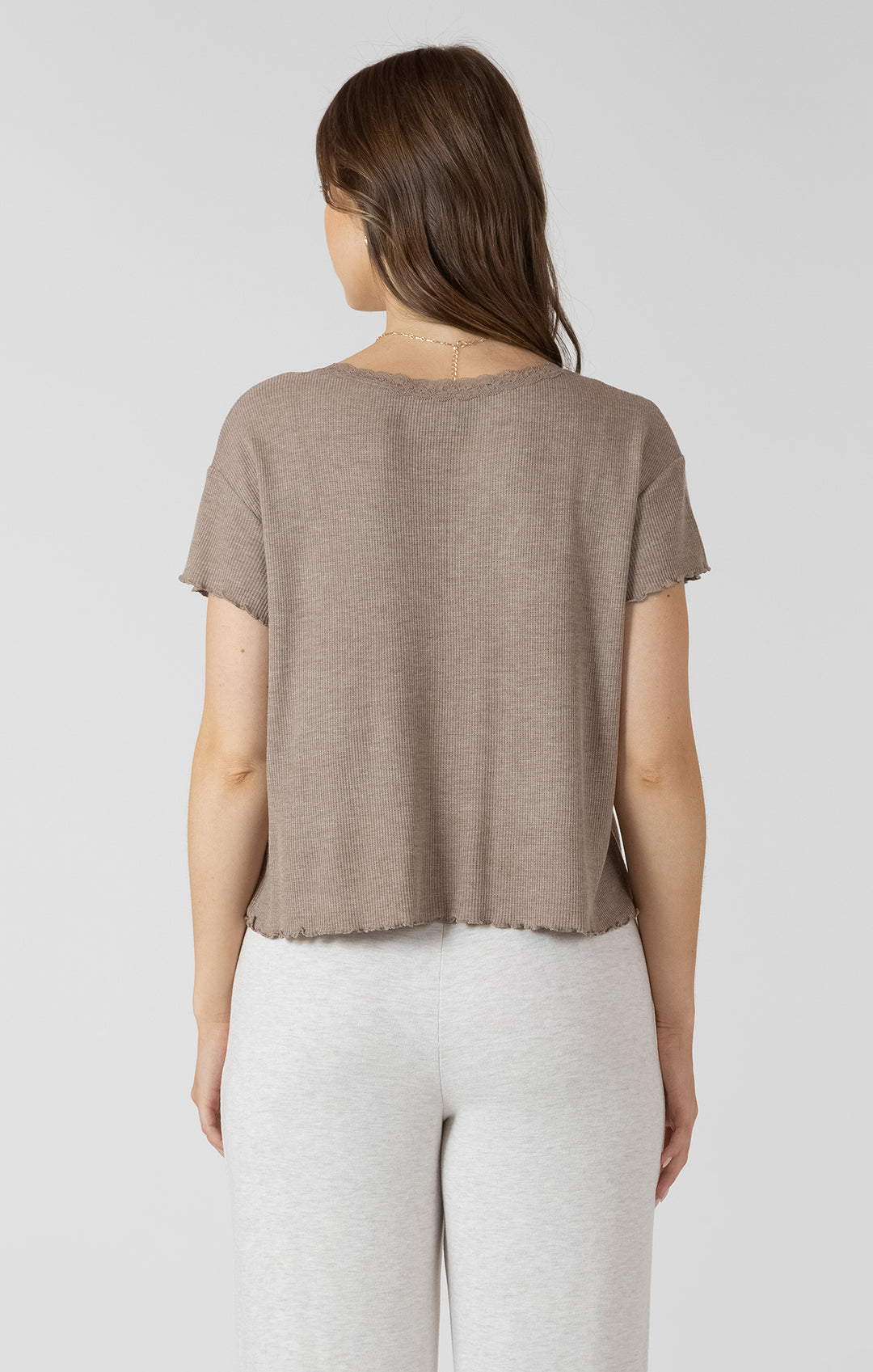 Woman wearing a brown t-shirt and white pants on a light gray background