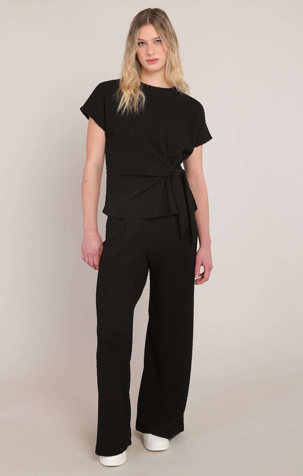 Woman wearing a black jumpsuit against a beige background