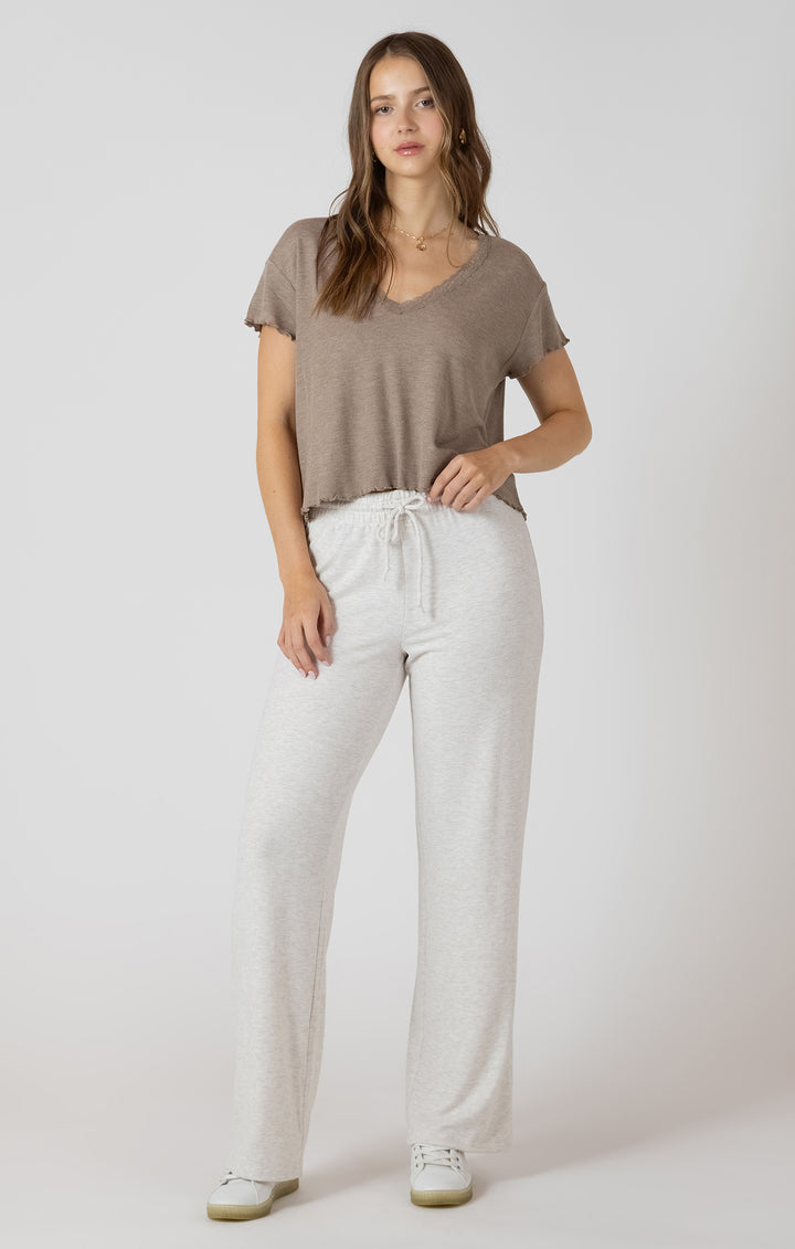 Woman wearing a brown t-shirt and white pants on a plain background