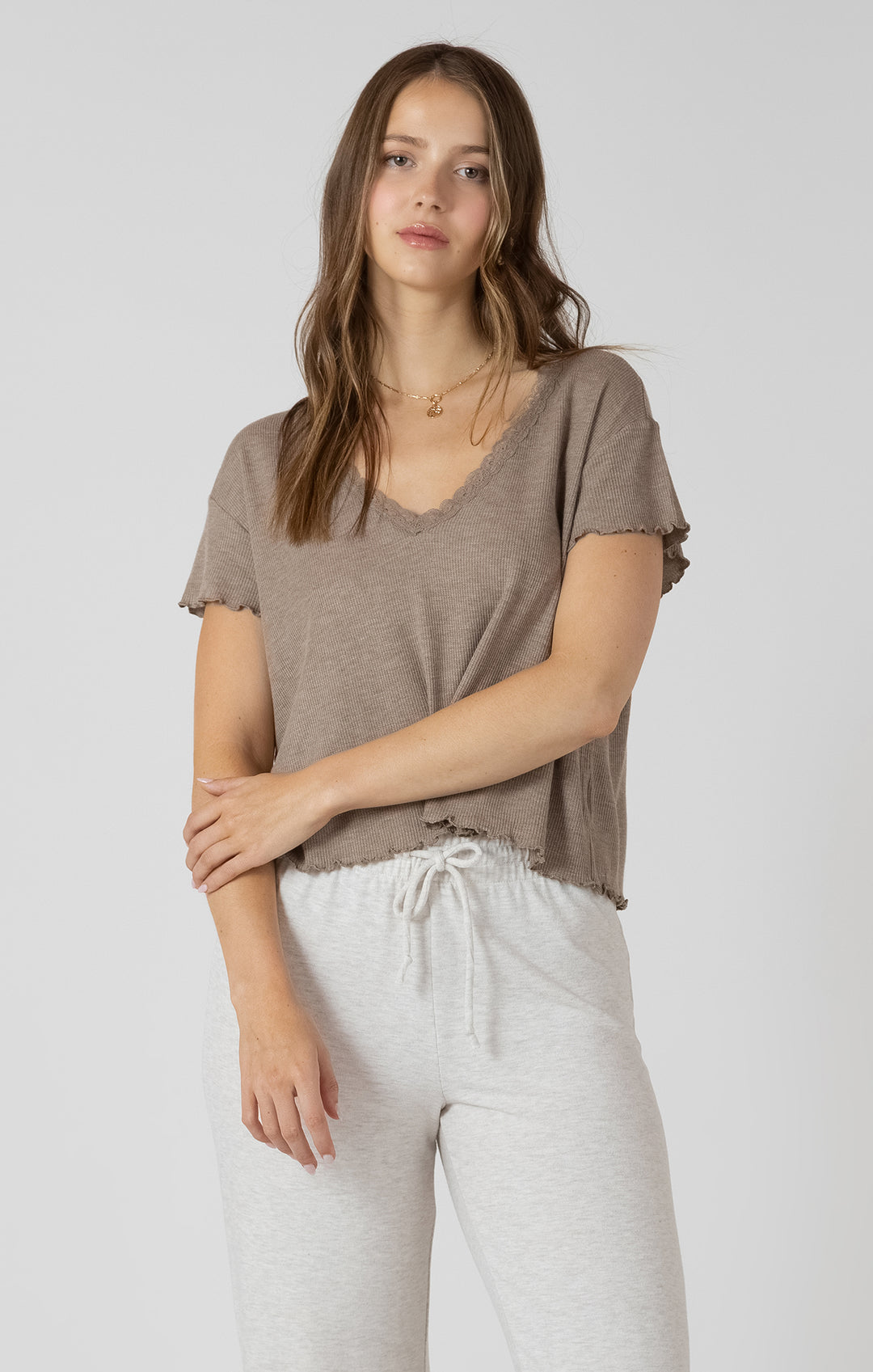 Woman wearing a brown t-shirt and white pants on a plain background