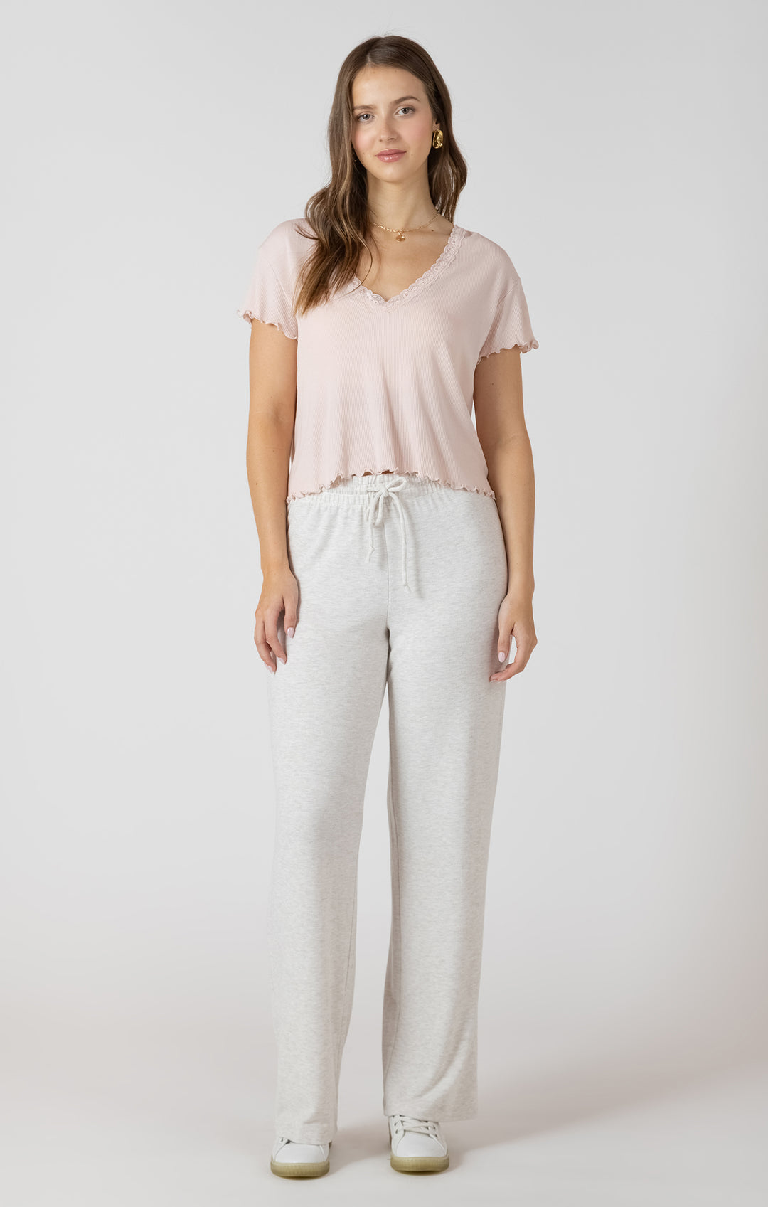 Woman wearing a light pink t-shirt and white pants on a plain background