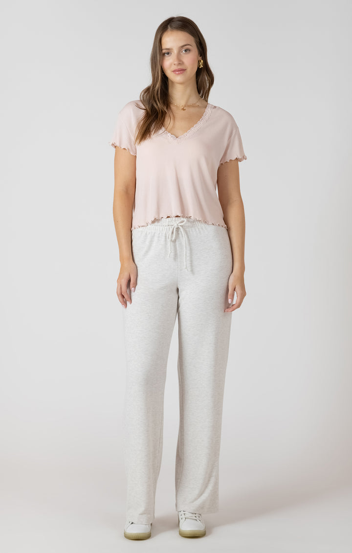 Woman wearing a light pink t-shirt and white pants on a plain background