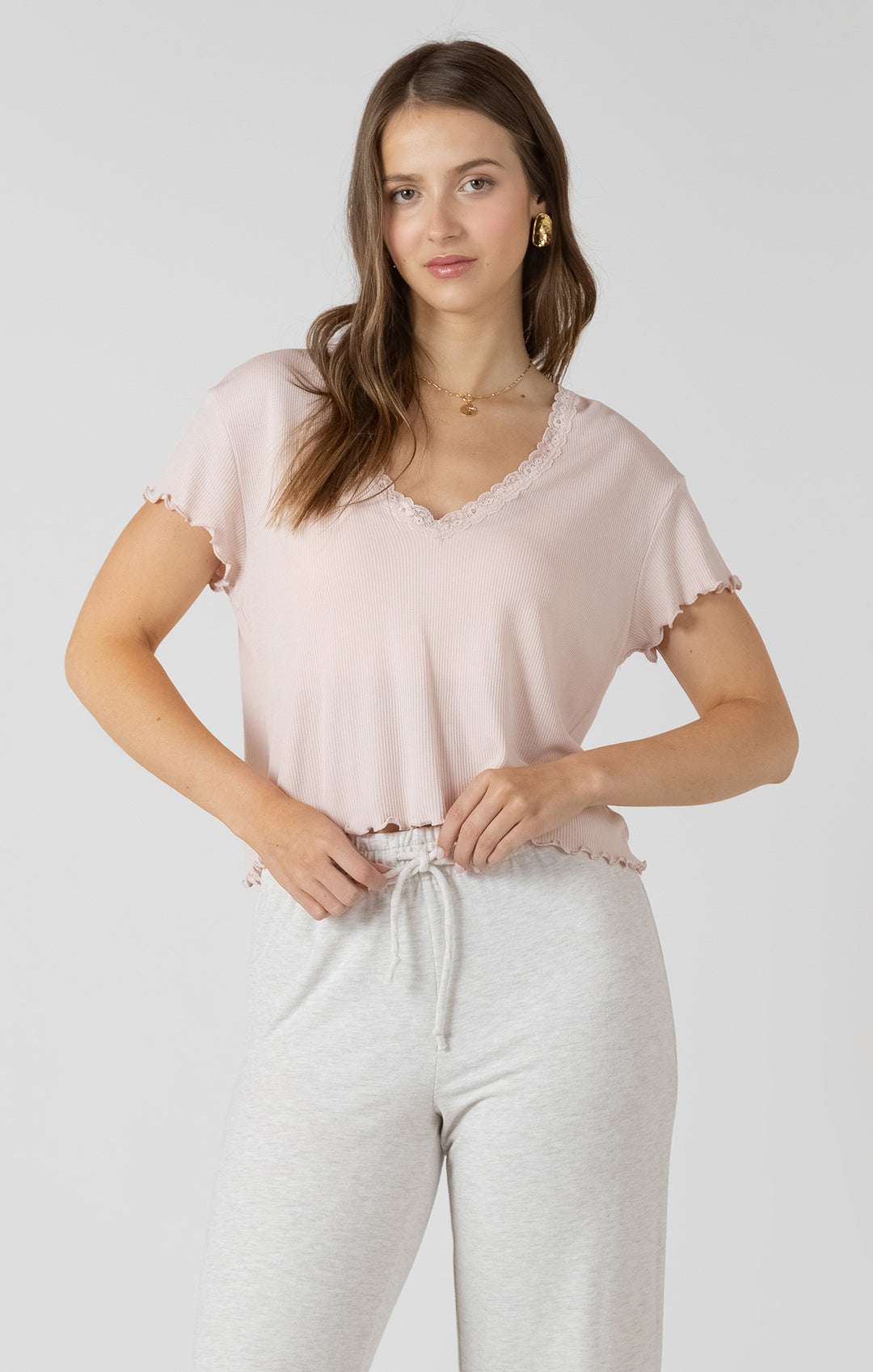 Woman wearing a light pink top and white pants on a plain background