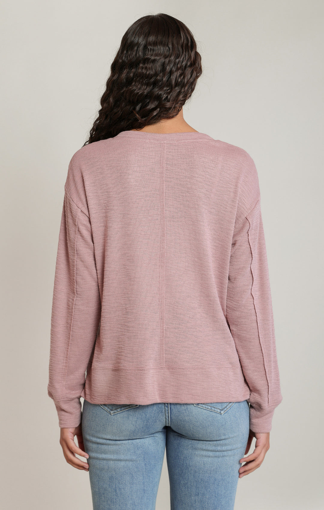 Person wearing a pink long-sleeve top and blue jeans on a plain background