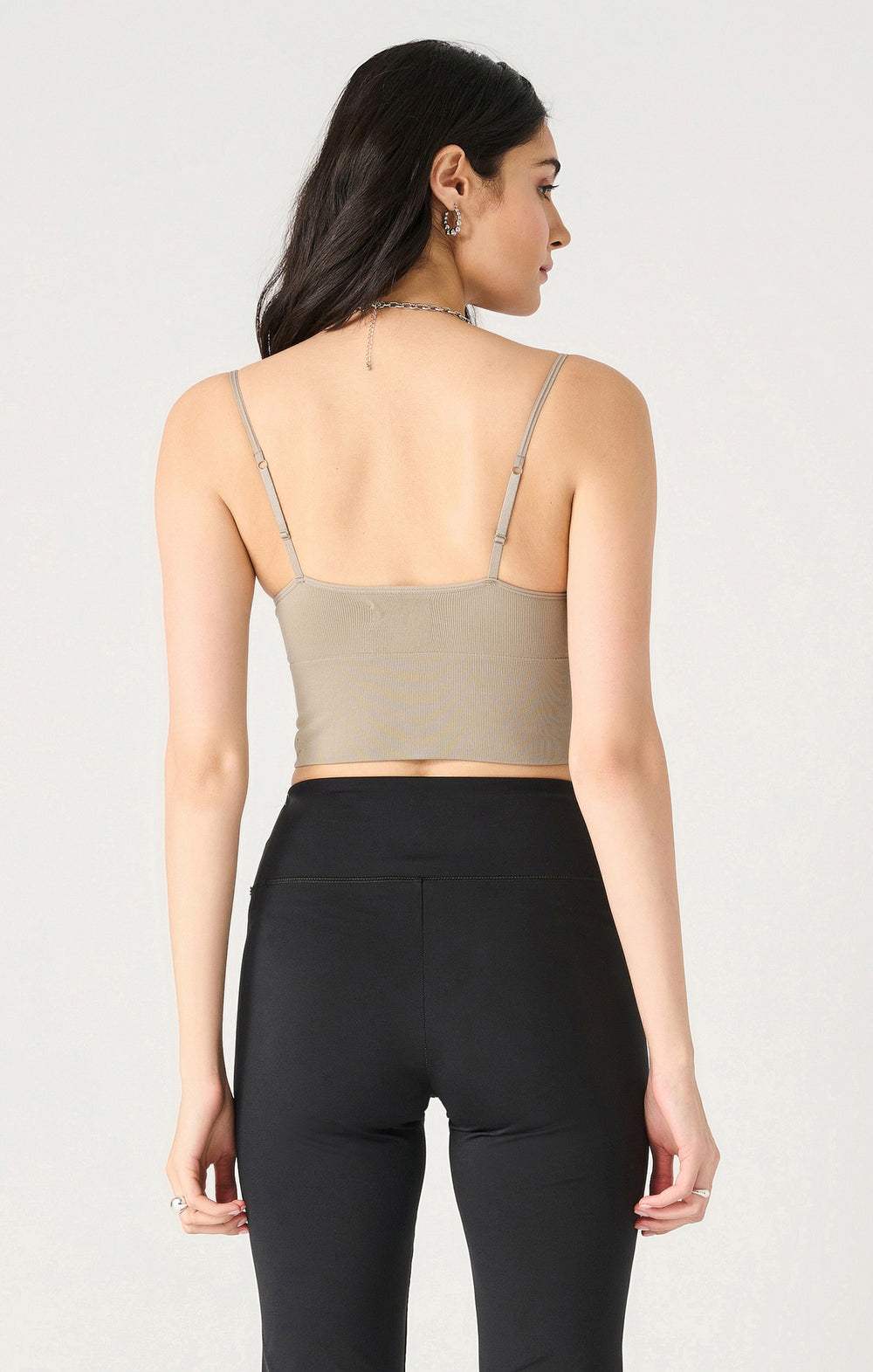 Woman wearing a beige crop top and black leggings on a light gray background