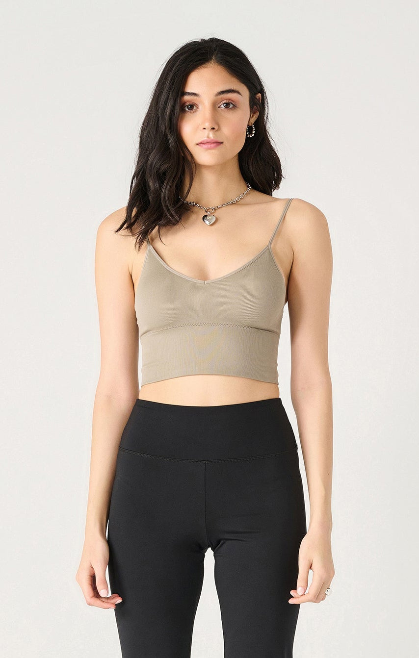Woman wearing a beige tank top and black flared pants on a white background