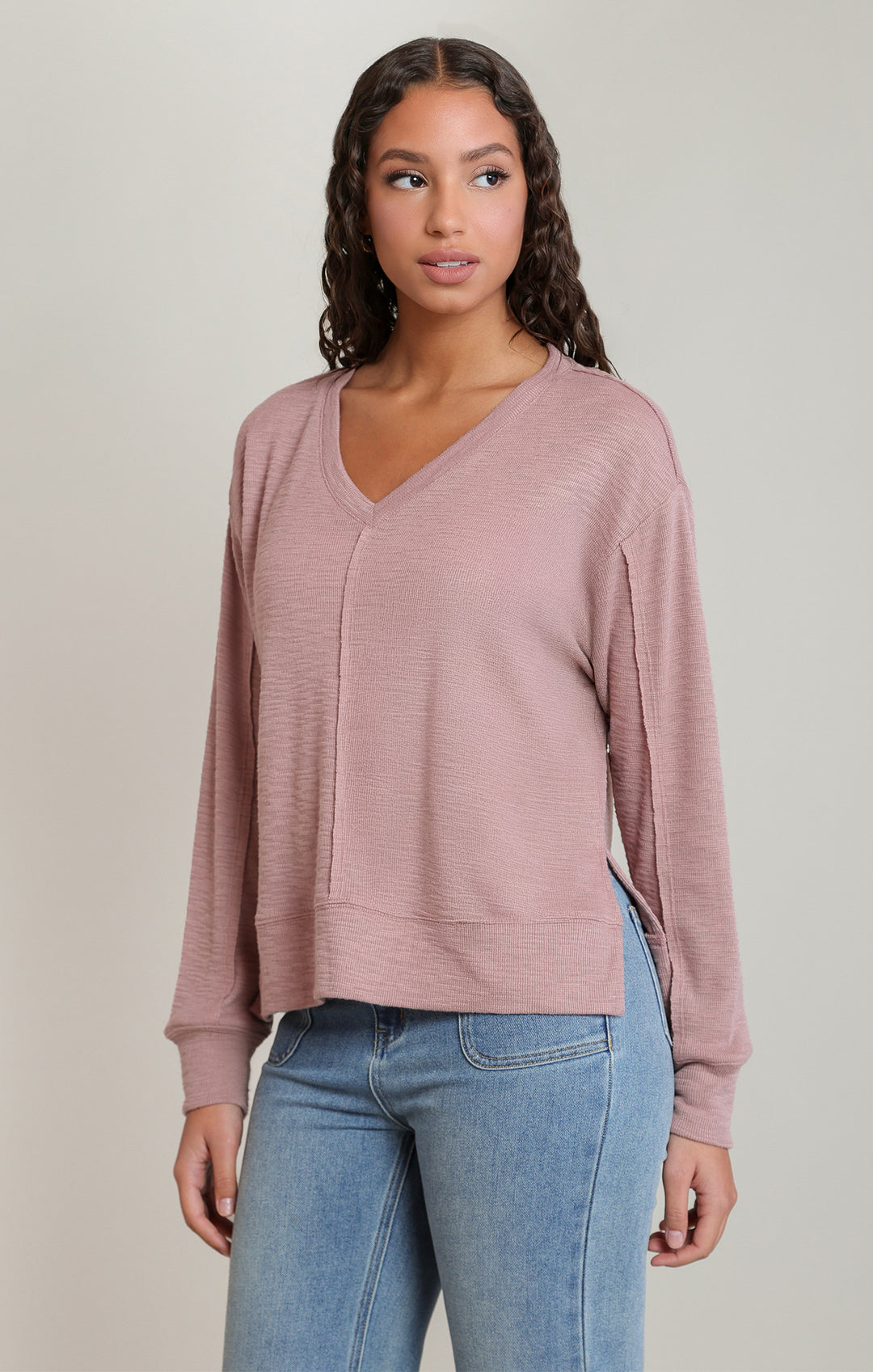 Woman wearing a pink long-sleeve top and blue jeans on a neutral background