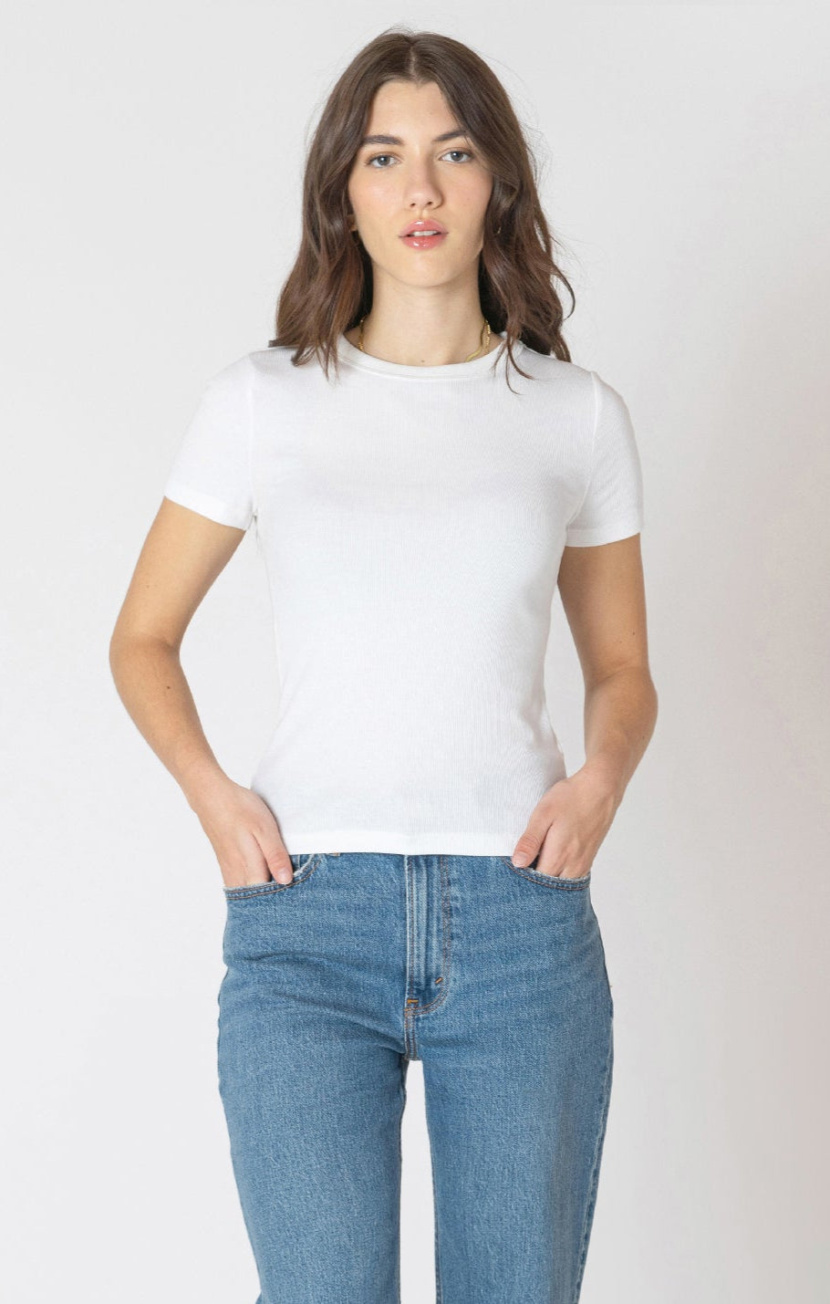 Woman wearing a white t-shirt and blue jeans against a plain background