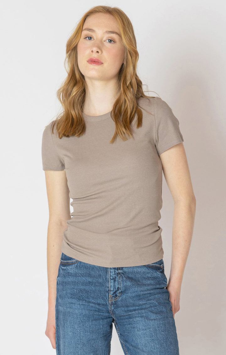 Woman wearing a beige t-shirt and blue jeans against a plain background