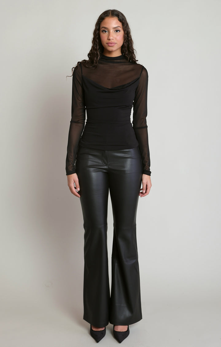 Woman wearing a black outfit with a sheer top and leather pants on a plain background