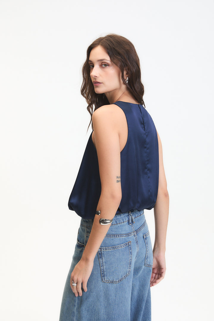 Woman wearing a navy sleeveless top and blue jeans on a white background