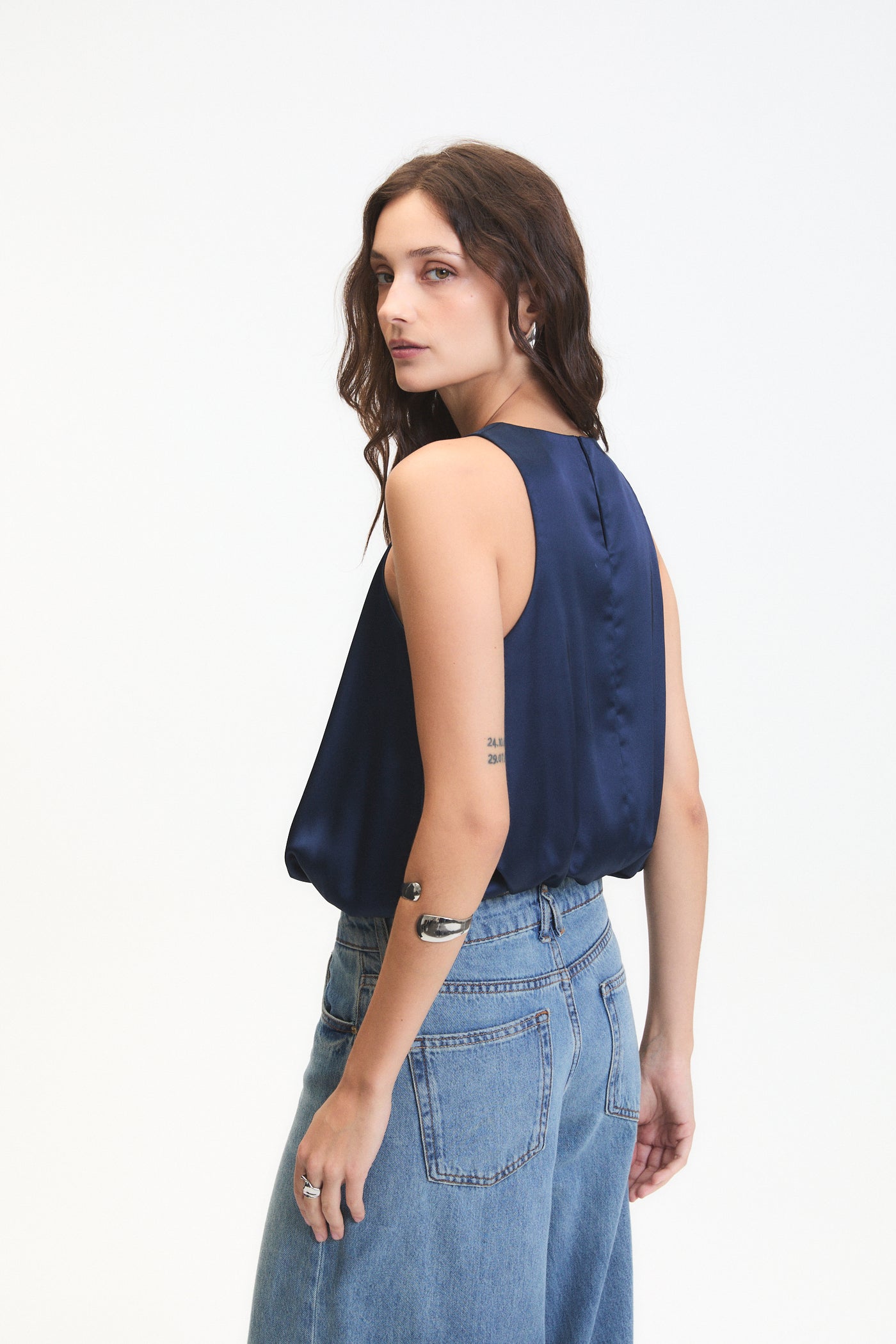 Woman wearing a navy sleeveless top and blue jeans on a white background