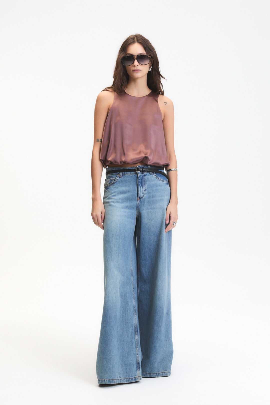 Woman wearing a sleeveless top and wide-leg jeans on a white background