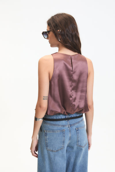 Woman wearing a sleeveless brown top and blue jeans on a white background