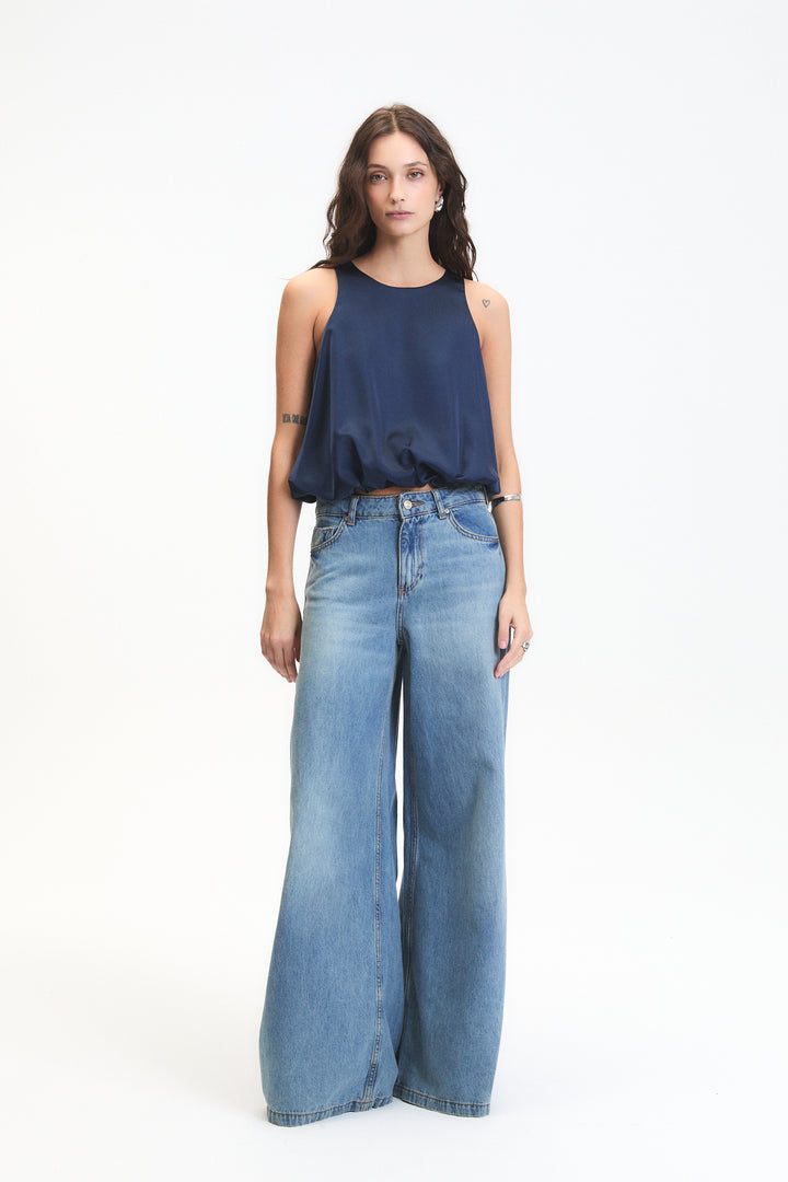 Woman wearing a navy sleeveless top and wide-leg jeans on a white background