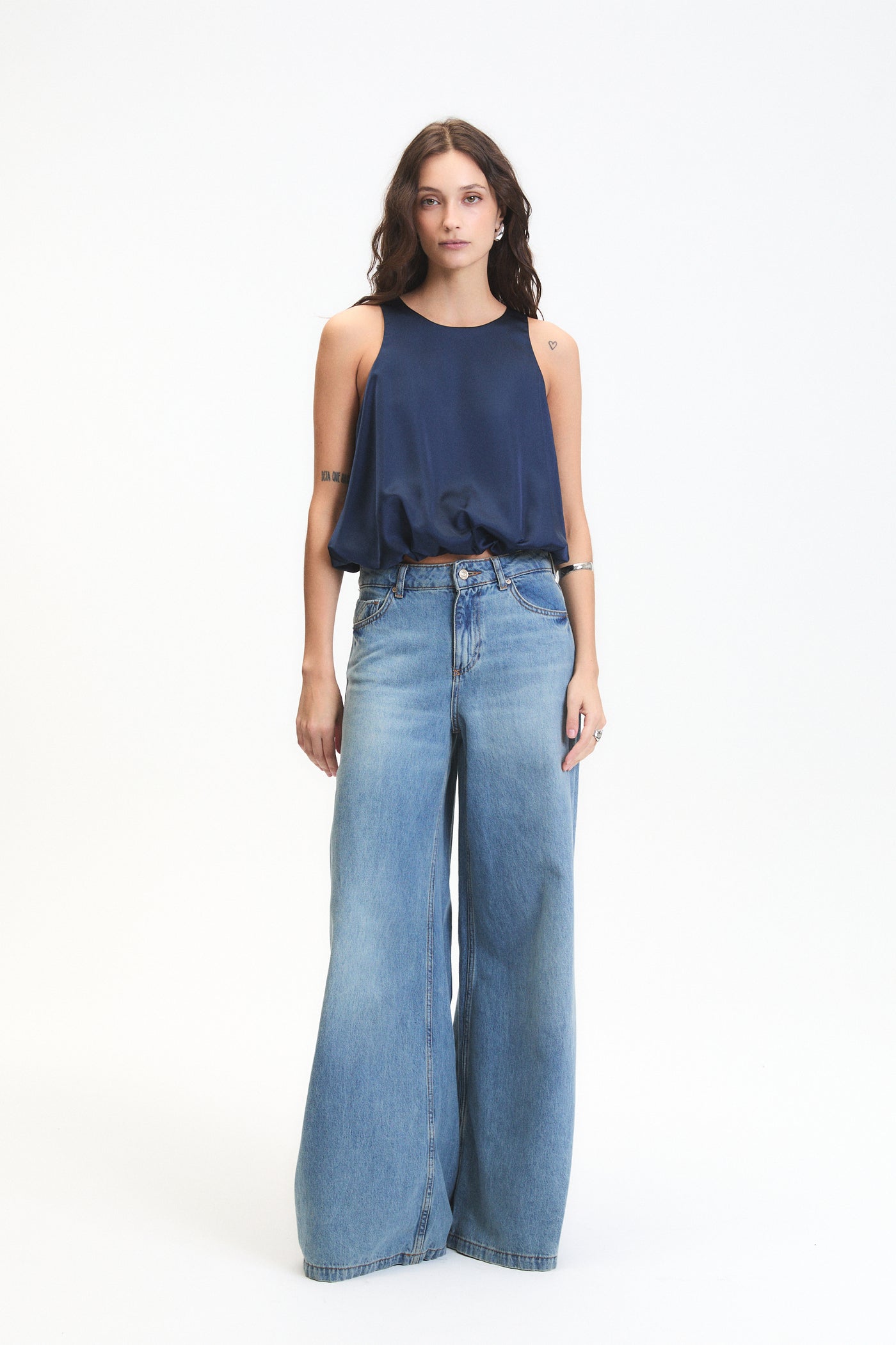 Woman wearing a navy sleeveless top and wide-leg jeans on a white background