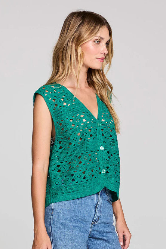 Woman wearing a green sleeveless crochet top and denim shorts on a gray background