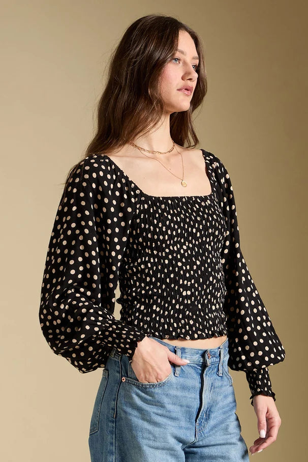 Woman wearing a black polka dot blouse and blue jeans against a beige background