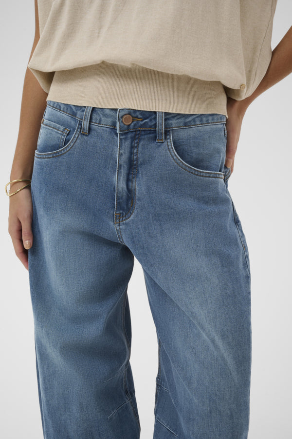Person wearing blue jeans and a beige top on a white background