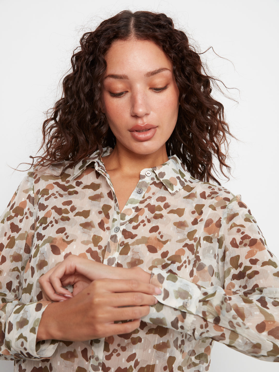 A woman wearing a long-sleeve button-up blouse with a brown and beige animal print pattern, shown against a plain light background.