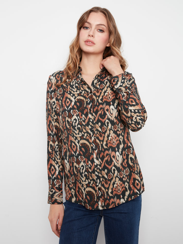A woman modeling a long-sleeve button-up blouse with an abstract, multicolor ikat-style pattern in black, brown, and beige, paired with dark blue jeans against a plain white studio background.