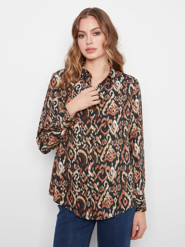 A woman wearing a long-sleeve button-up blouse with an abstract brown, beige, and black pattern, paired with dark blue jeans, photographed against a plain light gray background.