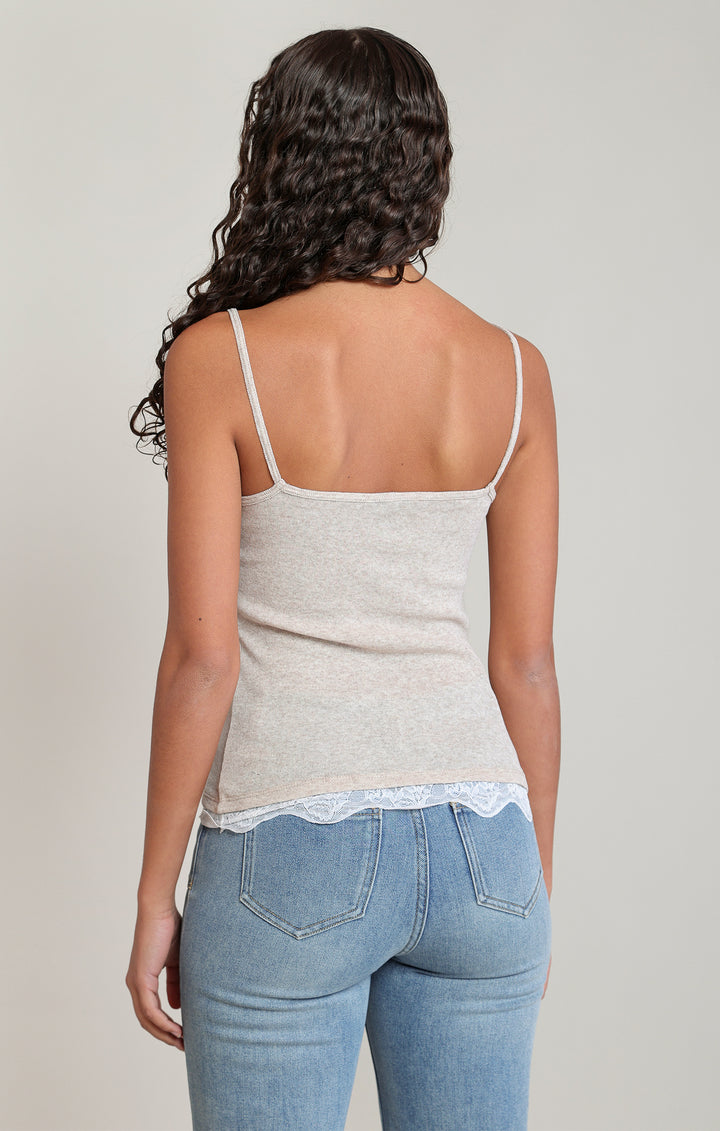 Woman wearing a beige tank top and blue jeans against a plain background
