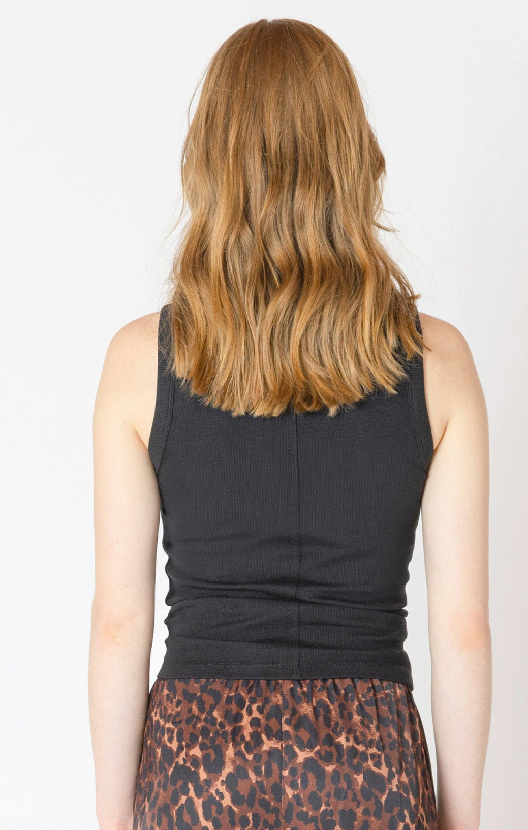 Person wearing a black sleeveless top and leopard print pants on a plain background