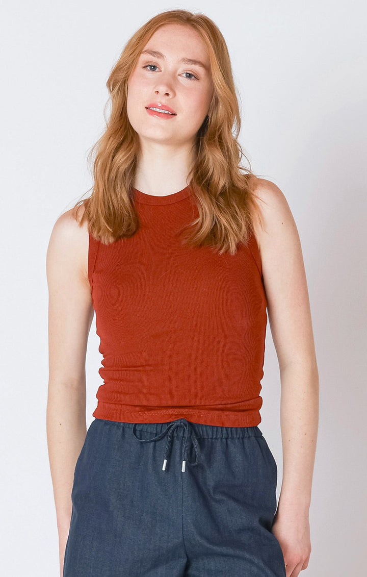 Woman wearing a red sleeveless top and blue pants against a plain background