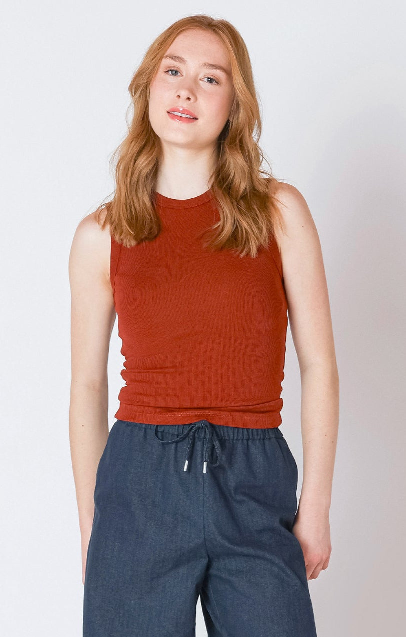 Woman wearing a rust-colored sleeveless top and blue pants against a plain background