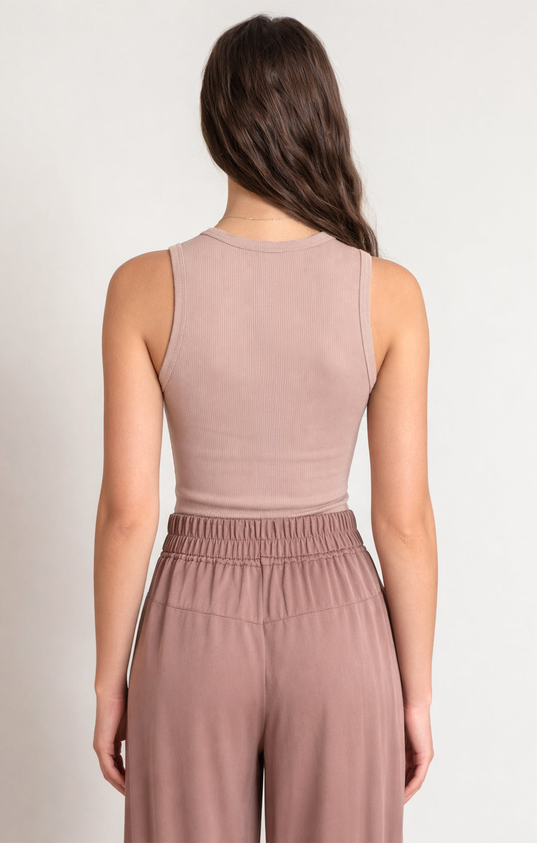 Woman wearing a matching mauve sleeveless top and high-waisted pants on a plain background