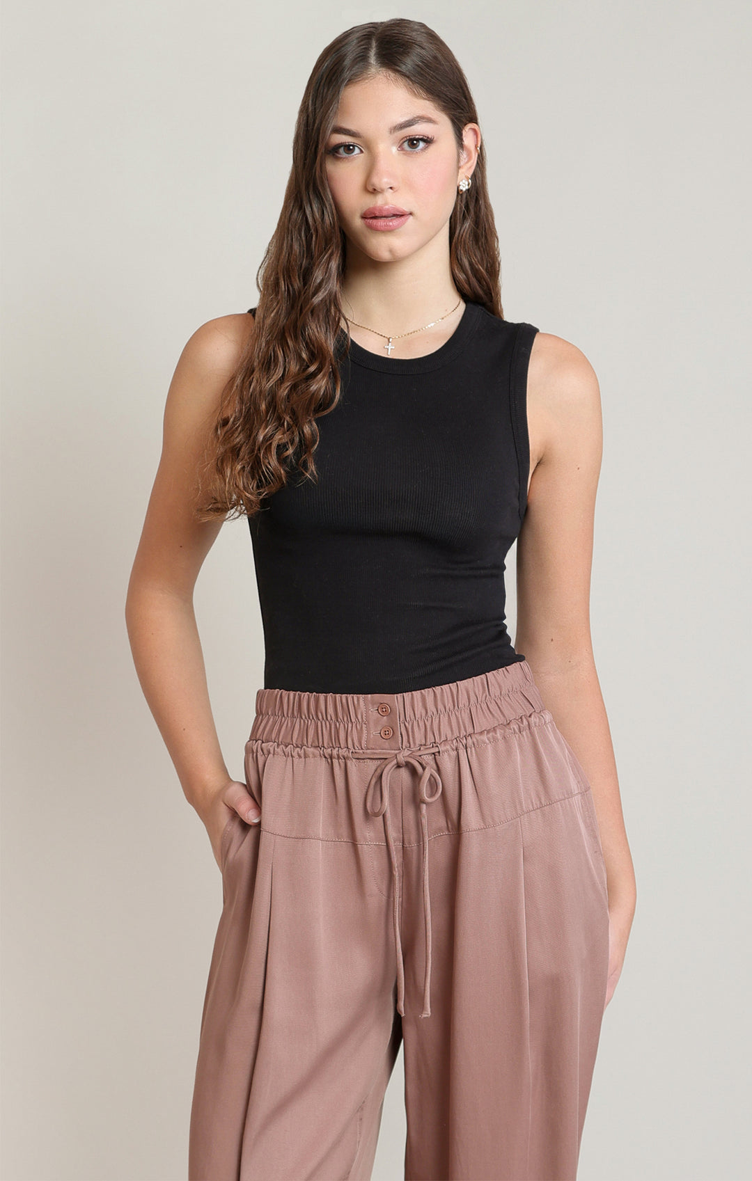 Woman wearing a black sleeveless top and pink pants against a plain background