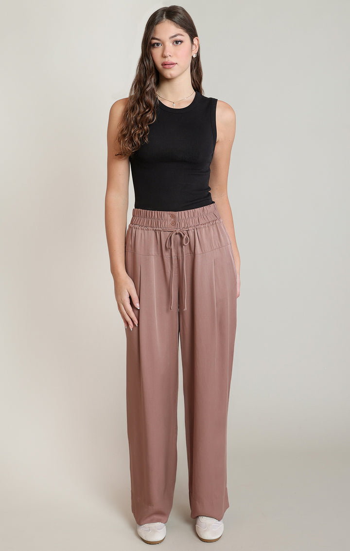 Woman wearing a black sleeveless top and brown wide-leg pants on a plain background