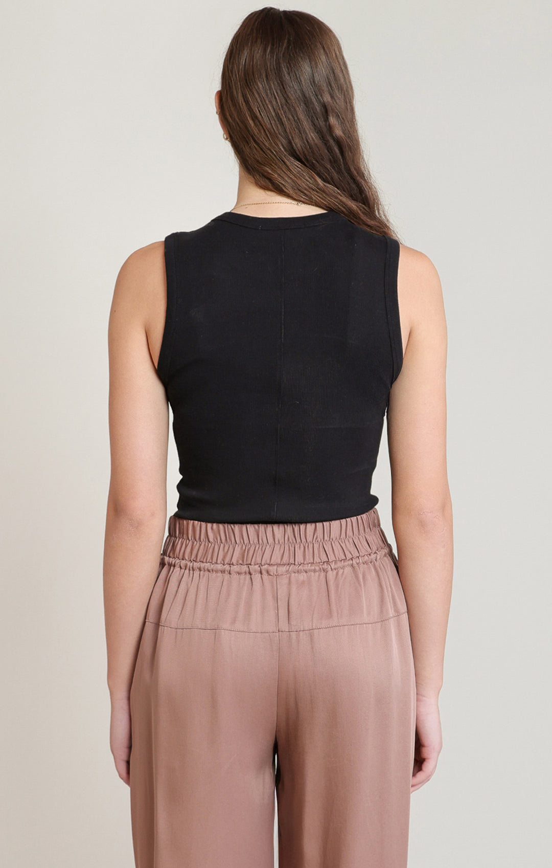 Woman wearing a black sleeveless top and brown pants on a plain background