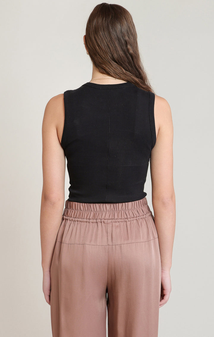 Woman wearing a black sleeveless top and brown pants on a plain background