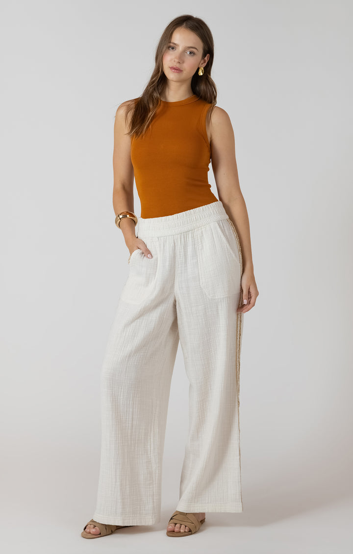 Woman wearing a mustard sleeveless top and white wide-leg pants on a plain background