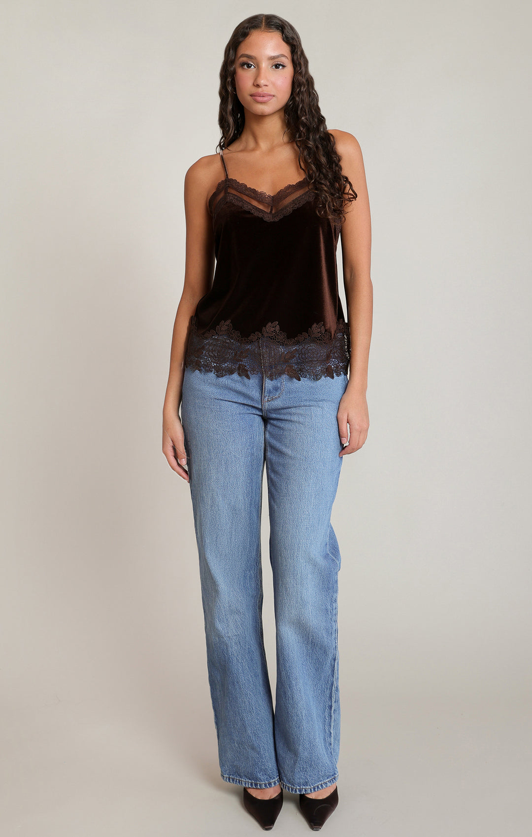 Woman wearing a black lace top and blue jeans on a plain background