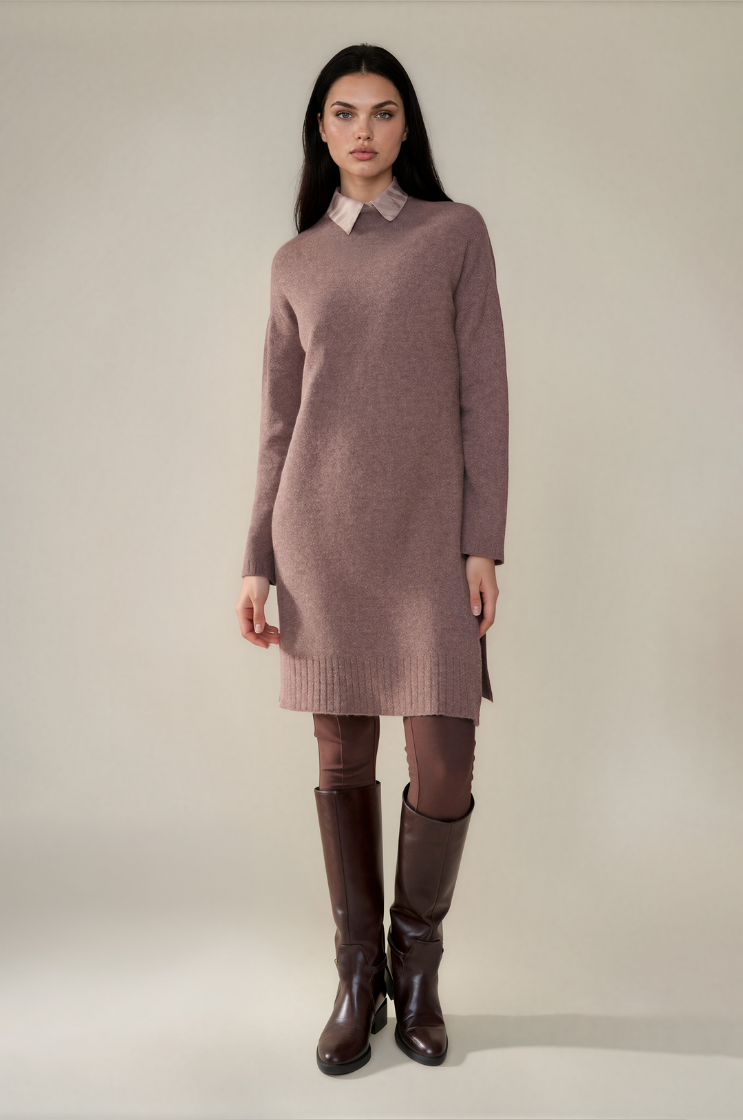 A model stands against a plain light beige studio background wearing a dusty mauve knit sweater dress with a contrasting light pink collar, paired with brown leggings and dark brown knee-high boots.
