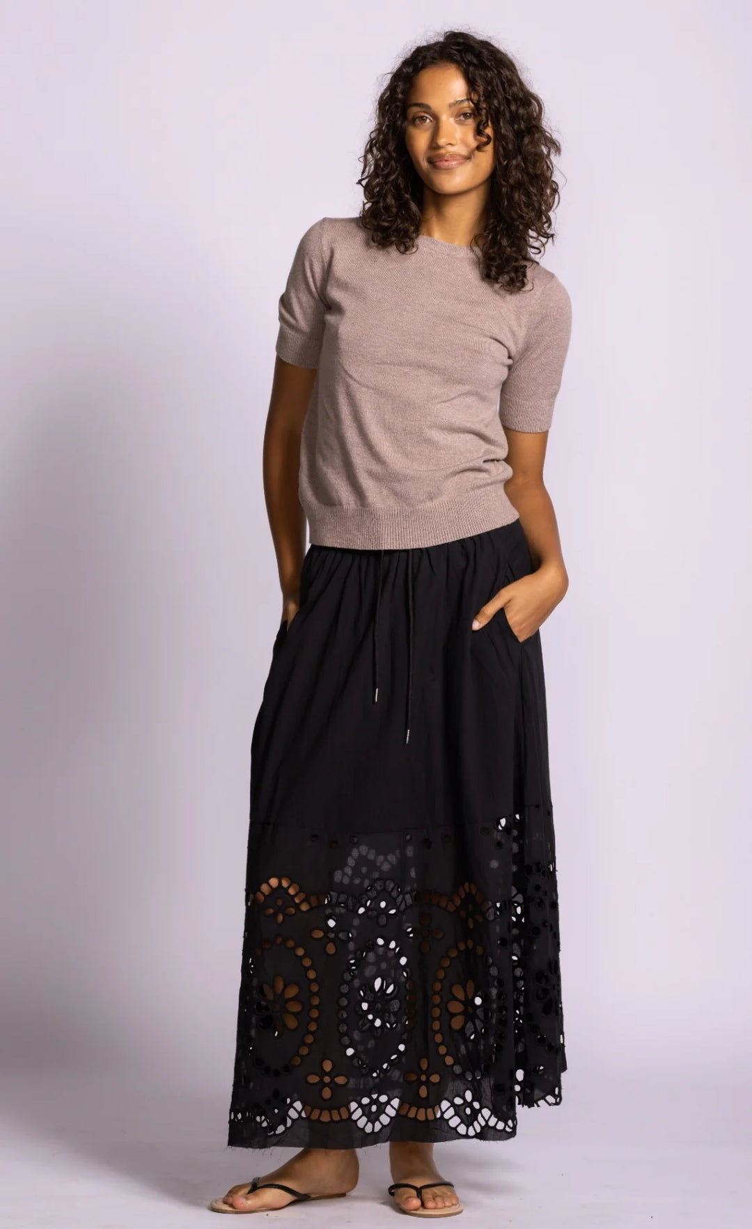 Woman wearing a beige top and black lace skirt on a white background